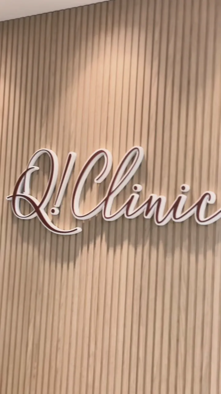 Letreiro Q!Clinic em letras claras sobre painel ripado de madeira, na entrada da clínica